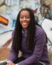 bettina love sitting in front of a mural wearing a purple sweater